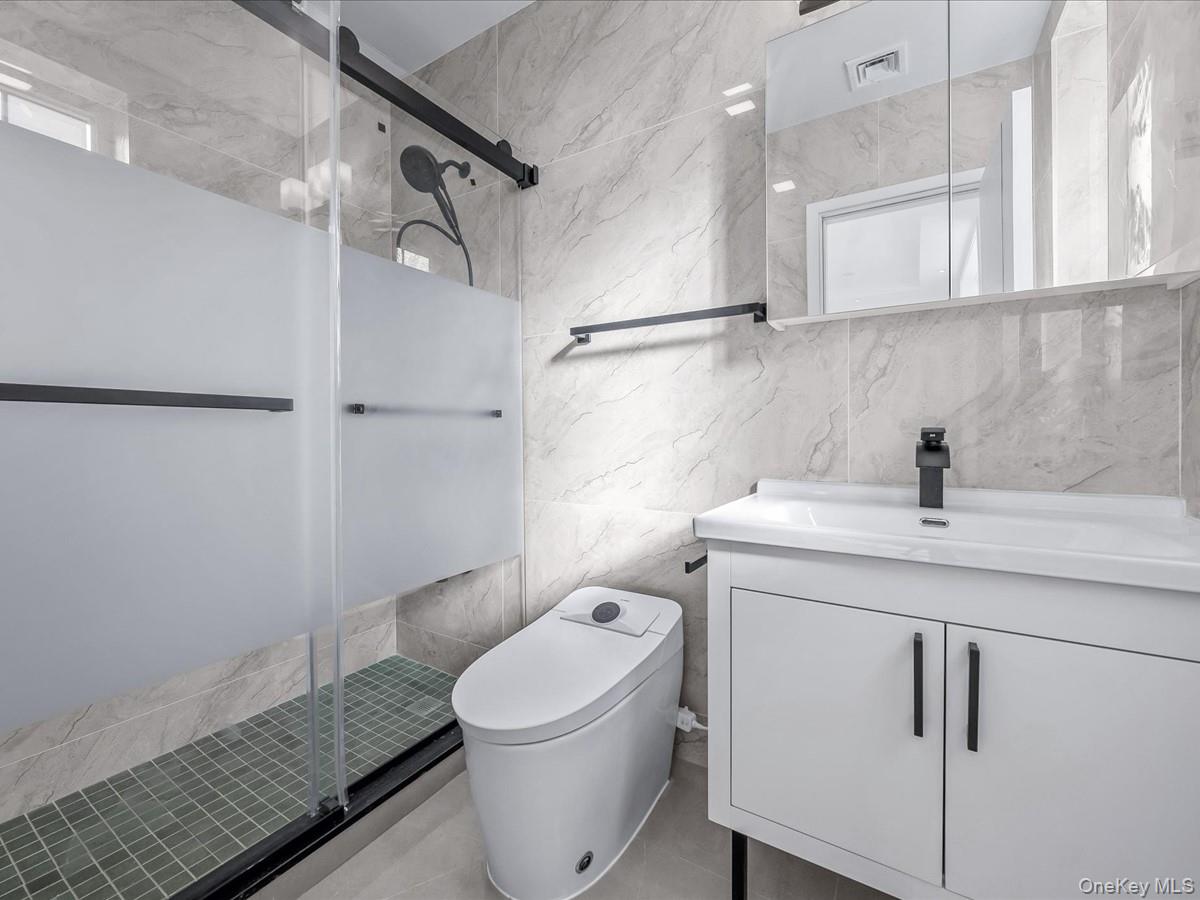 233-12 Bay Street Queens, NY 11363 - Photo 27 of 46 Full bathroom with tile walls, vanity, a shower stall, and light tile patterned floors