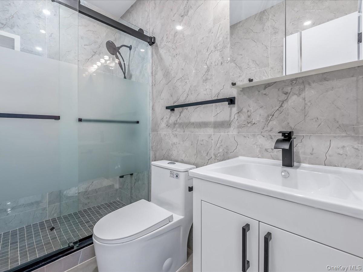 233-12 Bay Street Queens, NY 11363 - Photo 29 of 46 Full bathroom featuring tile walls, a shower stall, and vanity