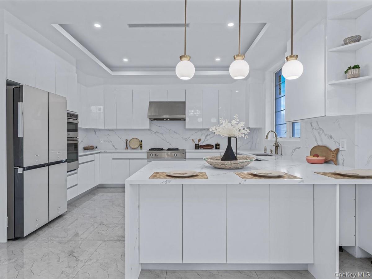 233-12 Bay Street Queens, NY 11363 - Photo 7 of 46 Kitchen featuring a peninsula, white cabinets, a tray ceiling, light stone countertops, and hanging light fixtures