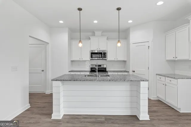 a large white kitchen with a large island oven a stove with wooden floors