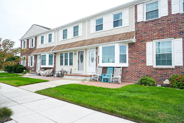 front view of a brick house with a yard and table and chairs with wooden fence