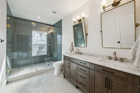 a spacious bathroom with double vanity sink a two mirror a window a bathtub and a glass door shower