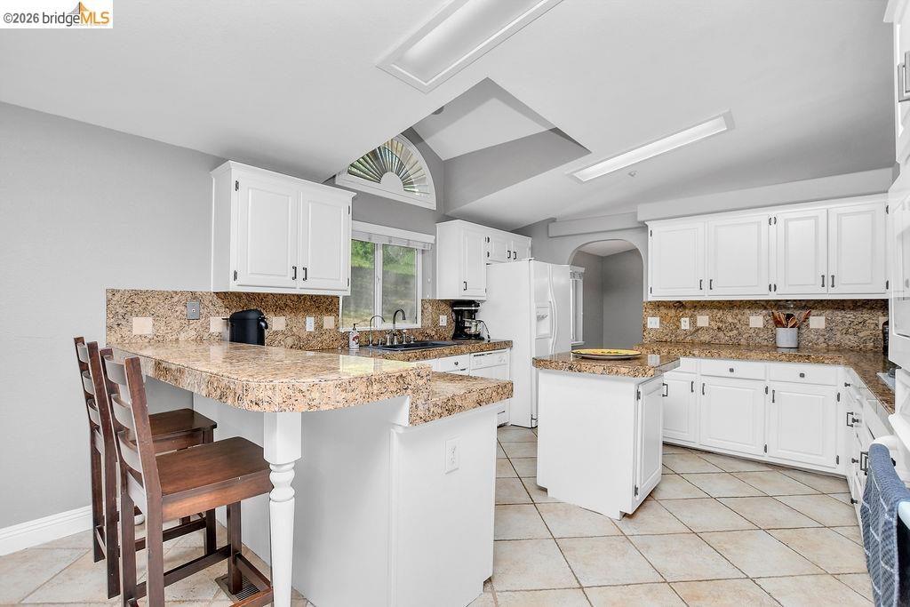 4229 Briones Valley Road Brentwood, CA 94513 - Photo 18 of 37 Kitchen featuring a center island, tasteful backsplash, white cabinets, vaulted ceiling, and a kitchen bar