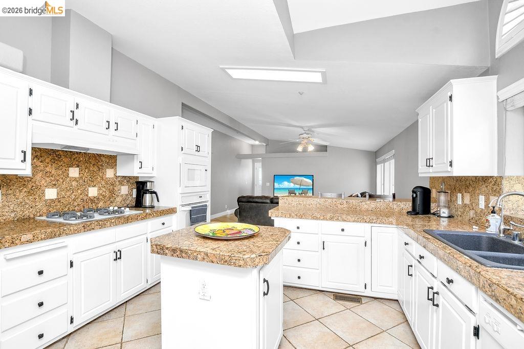 4229 Briones Valley Road Brentwood, CA 94513 - Photo 20 of 37 Kitchen featuring decorative backsplash, tile counters, white cabinetry, light tile patterned floors, and vaulted ceiling