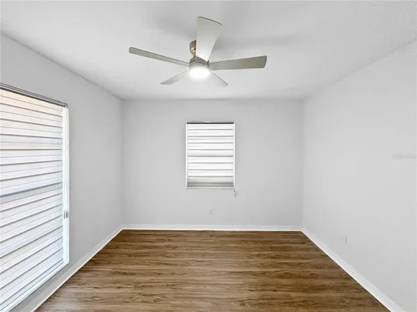 an empty room with wooden floor fan and windows