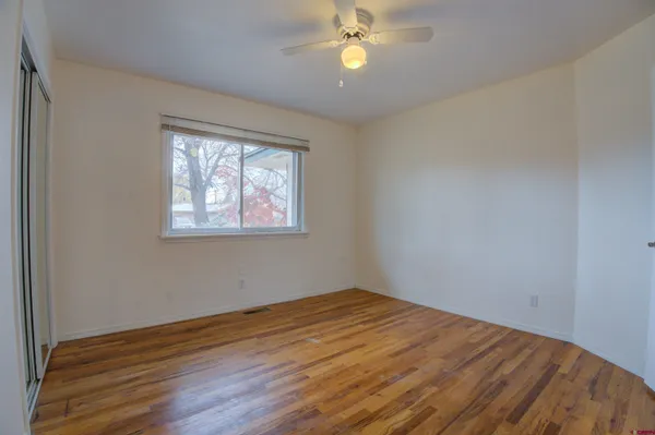 an empty room with wooden floor fan and windows