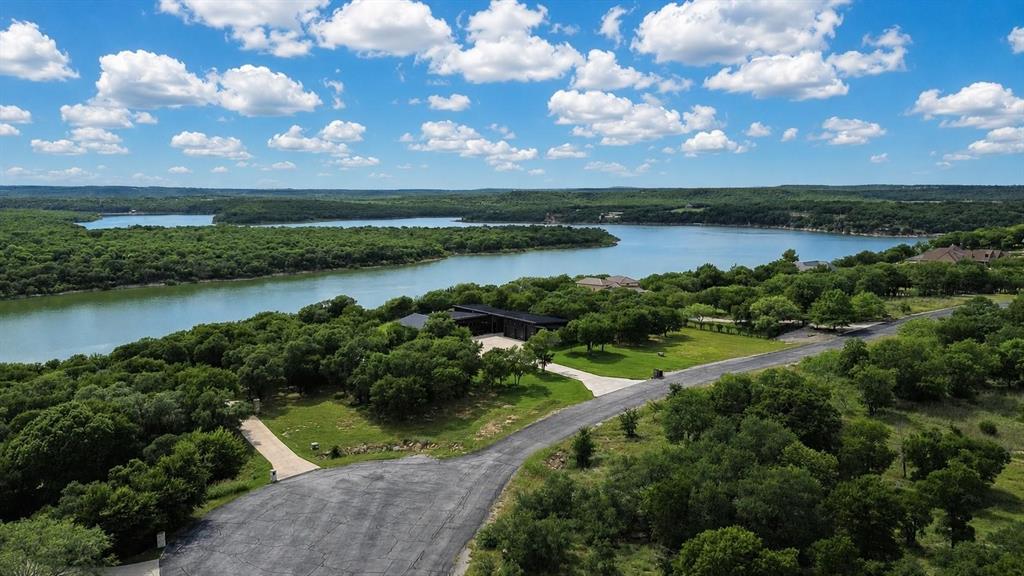 274 Ridgeline Drive Chico, TX 76431 - Photo 1 of 8 Expansive waterfront property featuring a modern residence, lush surrounding trees, and a paved driveway