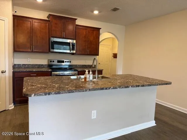 a kitchen with granite countertop a sink a stove top oven a counter space and cabinets