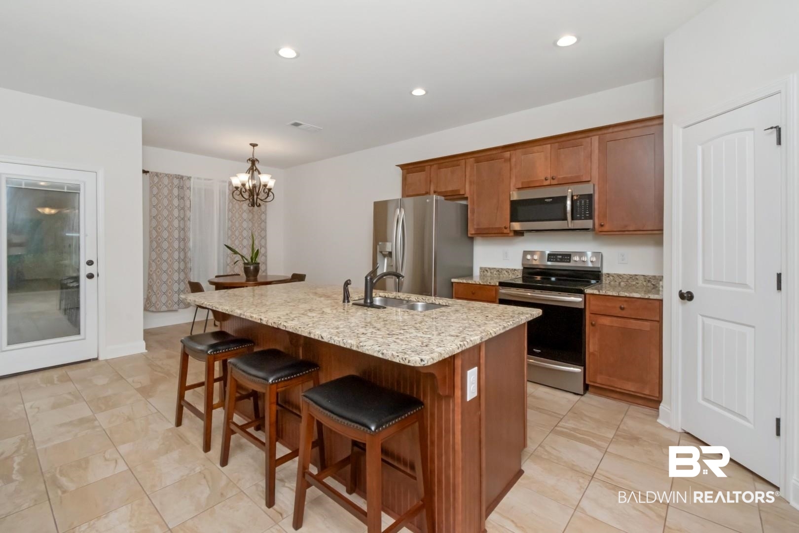 10714 Brodick Loop Spanish Fort, AL 36527 - Photo 5 of 26 Kitchen with appliances with stainless steel finishes, brown cabinetry, a chandelier, an island with sink, and light stone countertops