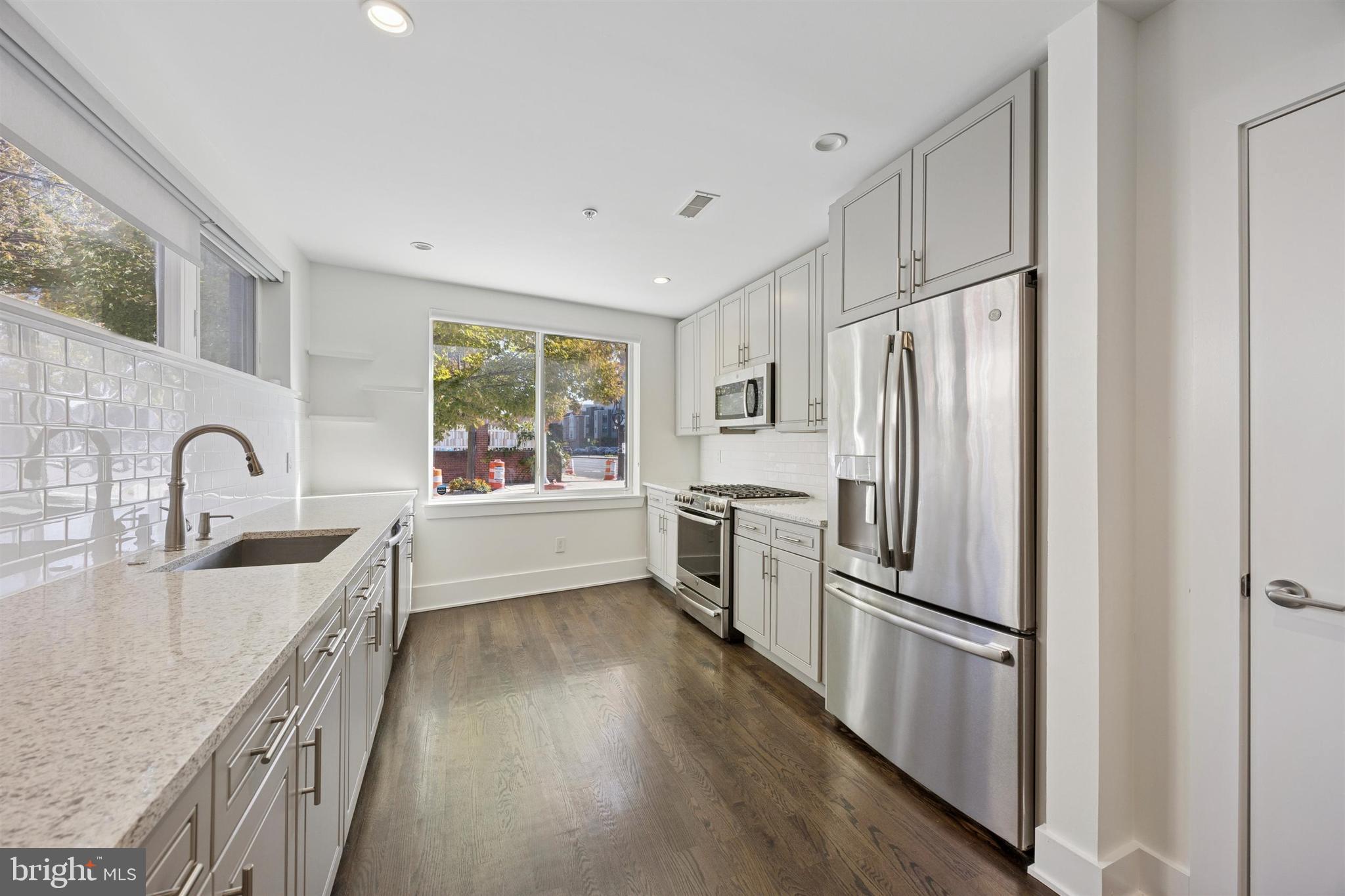 a kitchen with stainless steel appliances granite countertop a refrigerator a sink a stove and white cabinets with wooden floor