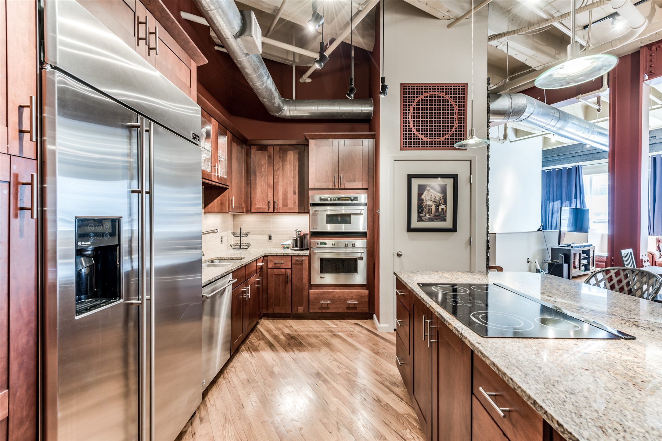 705 Main Street, Unit 215 Houston, TX 77002 - Photo 2 of 36 This modern kitchen features stainless steel appliances, wood cabinetry, and a spacious granite island with an electric cooktop.