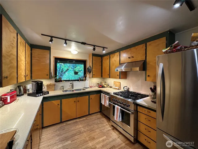 a kitchen with stainless steel appliances a stove a sink dishwasher a refrigerator and a dining table with wooden floor