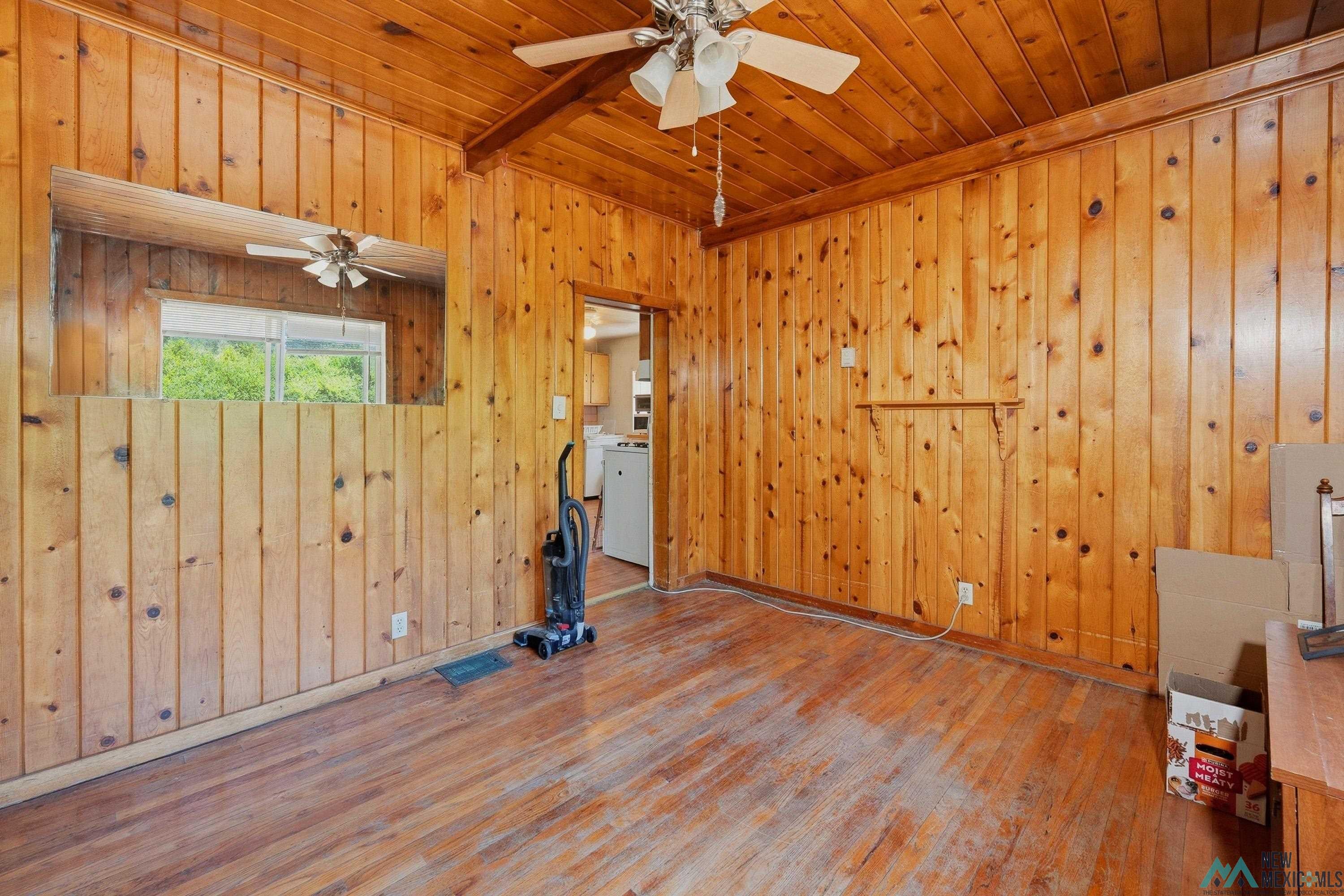 811 North 4th Street Raton, NM 87740 - Photo 6 of 26 Room featuring extensive wood paneling, wood-finish flooring, a ceiling fan, and a transom window providing natural light