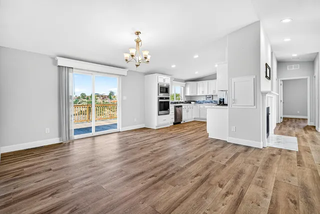 a view of an empty room and kitchen with wooden floor