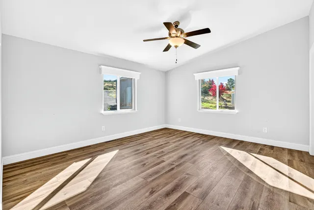 an empty room with wooden floor chandelier fan and windows