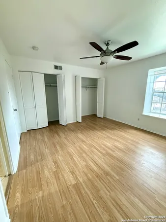 an empty room with wooden floor ceiling fan and windows