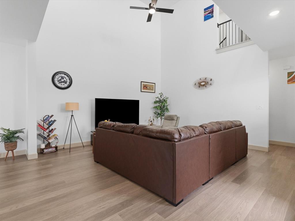 9533 Keep Street Frisco, TX 75035 - Photo 12 of 40 Spacious living area featuring a vaulted ceiling, ceiling fan, wood-finish flooring, white walls, and a staircase with black metal balusters