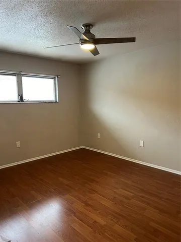 an empty room with wooden floor fan and windows