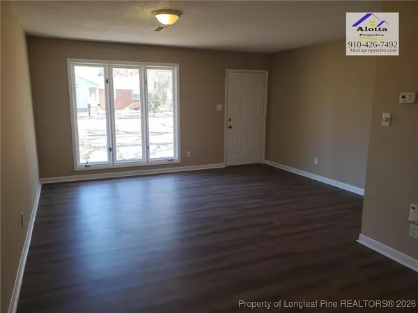 an empty room with wooden floor and windows with curtains