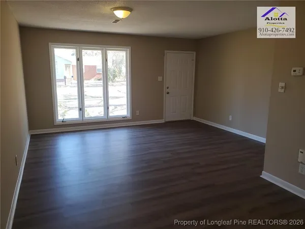 an empty room with wooden floor and windows with curtains