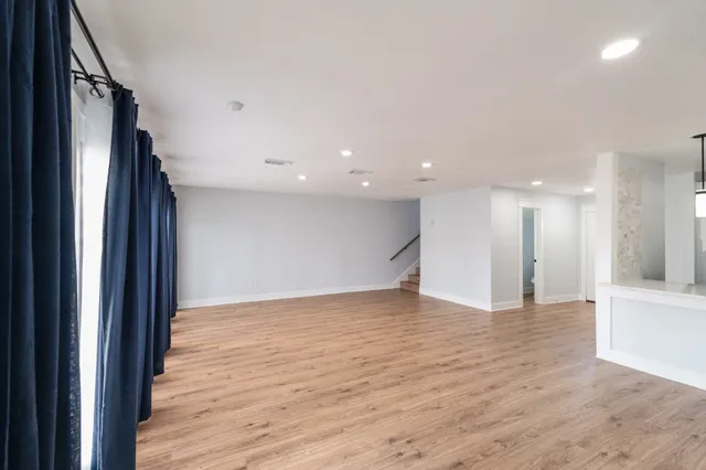 a view of an empty room with wooden floor and a kitchen
