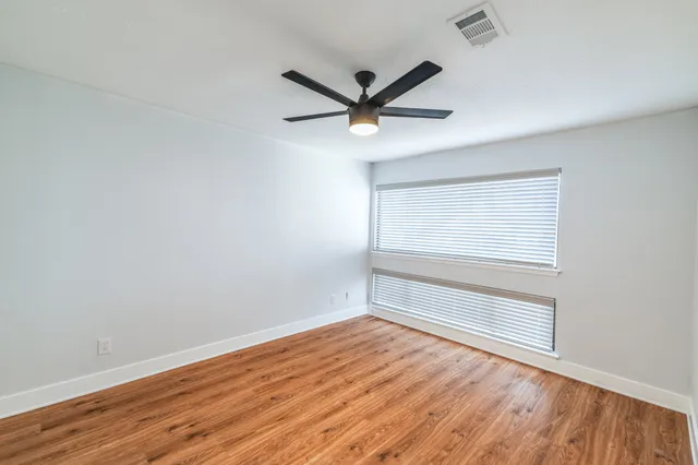 a view of an empty room with wooden floor and a ceiling fan