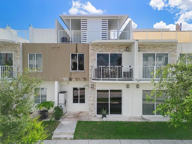 a view of a brick house with a yard plants and large tree