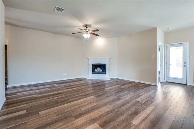 a view of an empty room with wooden floor and a ceiling fan