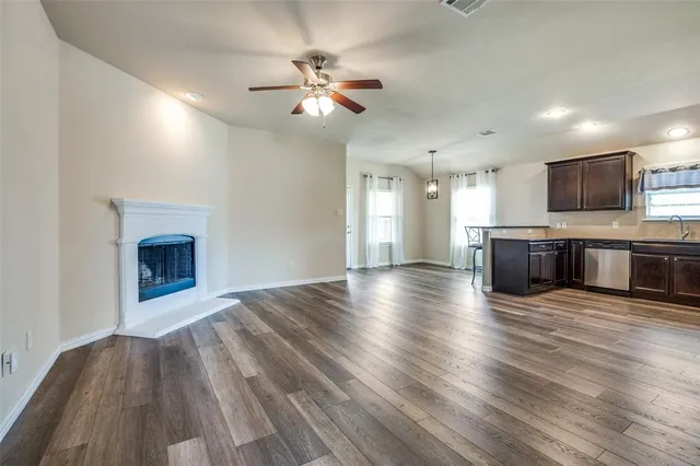 an empty room with wooden floor fireplace and kitchen view