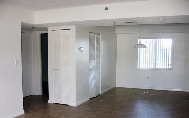 an empty room with wooden floor closet and windows