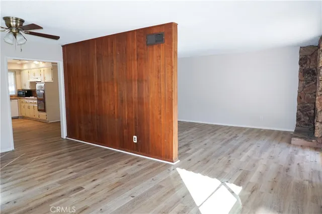 an empty room with wooden floor and way to kitchen