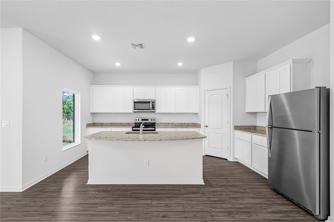 7926 105th Avenue Vero Beach, FL 32967 - Photo 6 of 18 a kitchen with stainless steel appliances granite countertop a refrigerator a stove a sink dishwasher and a refrigerator with wooden floor