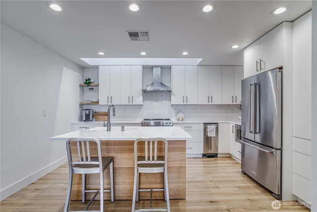a kitchen with kitchen island stainless steel appliances a refrigerator and a stove top oven with wooden floor