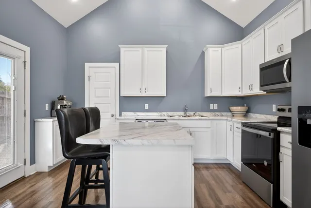 a kitchen with stainless steel appliances kitchen island granite countertop a sink dishwasher a stove top oven a dining table and chairs with wooden floor