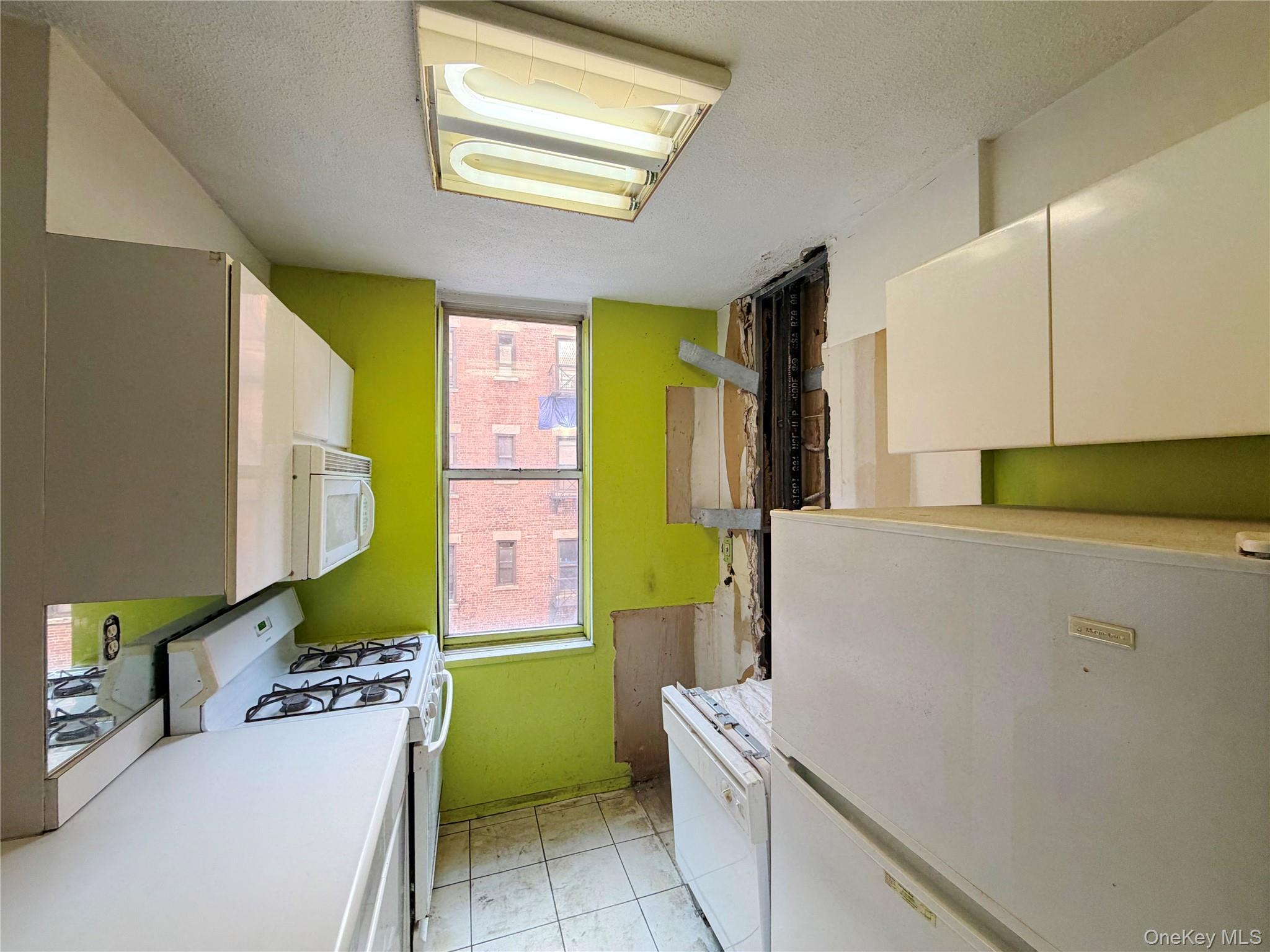 520 West 112th Street, Unit 4B Manhattan, NY 10025 - Photo 11 of 11 Kitchen with white appliances, white cabinetry, light countertops, and a textured ceiling