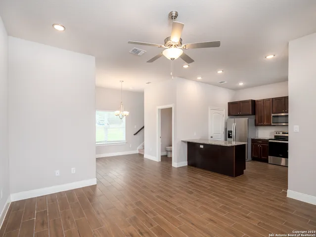 a view of an empty room and kitchen with wooden floor