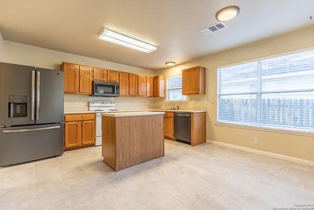 a kitchen with stainless steel appliances a refrigerator a sink a stove a microwave a center island and a window