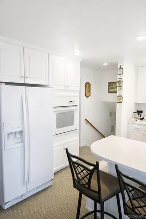 a large white kitchen with granite countertop a stove a sink a refrigerator and white cabinets with wooden floor