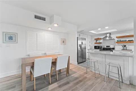 a kitchen with stainless steel appliances kitchen island granite countertop a dining table chairs and a refrigerator