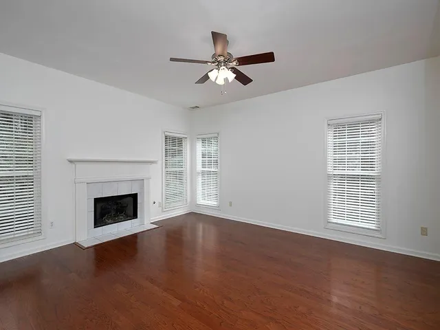 an empty room with wooden floor fireplace and windows