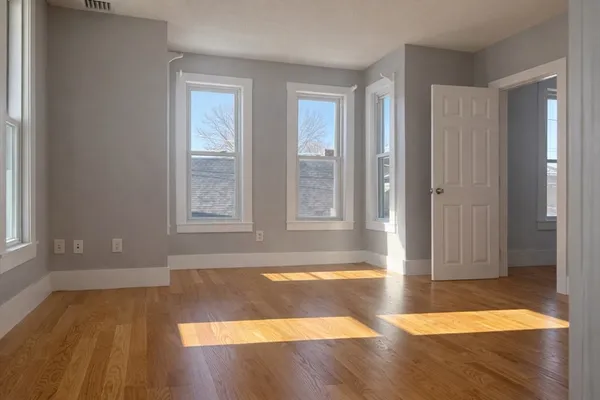 a view of an empty room with window and wooden floor