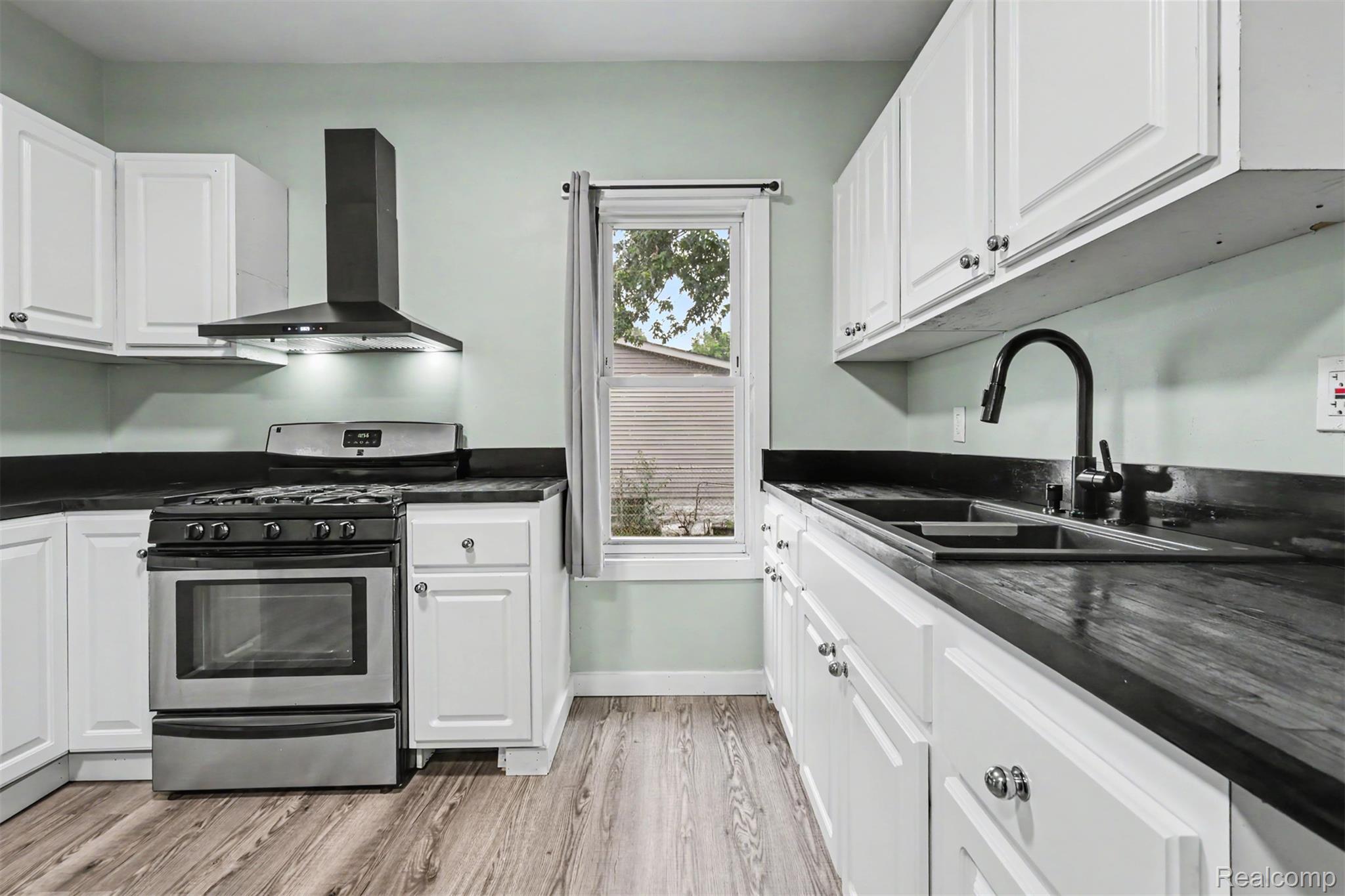 8397 Lane Street Detroit, MI 48209 - Photo 13 of 41 White cabinetry with dark countertops, wood-finish flooring, stainless steel range, and a black range hood