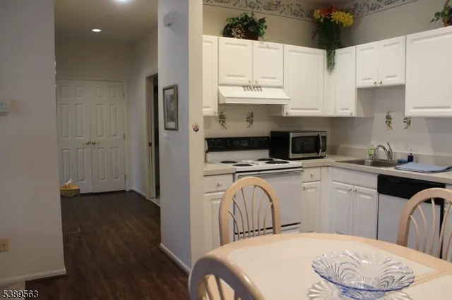 a kitchen with stainless steel appliances a white refrigerator a sink a stove and white cabinets with wooden floor