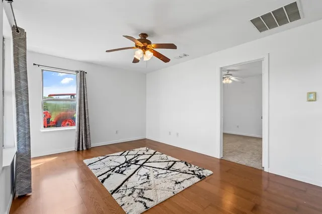 an empty room with wooden floor ceiling fan and window