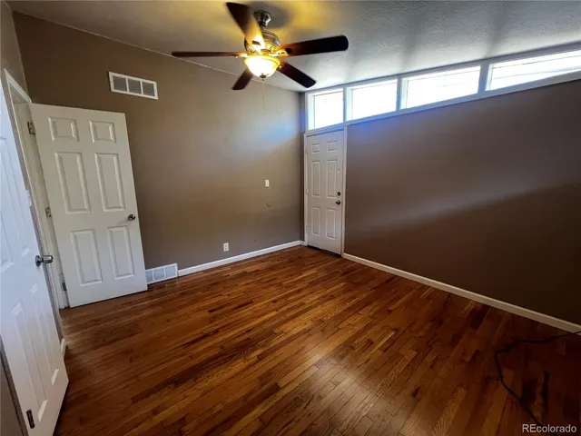 an empty room with wooden floor fan and windows