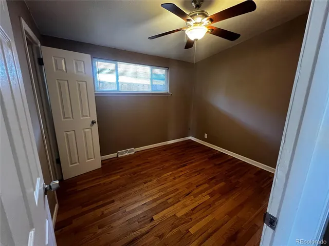 an empty room with wooden floor fan and windows