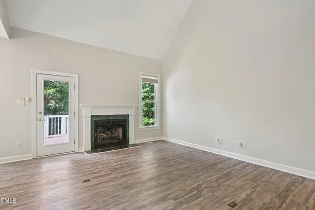 an empty room with wooden floor fireplace and windows