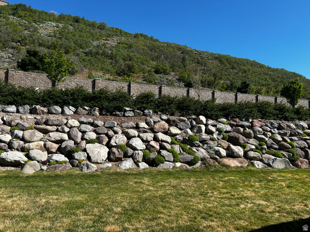 1154 Sunset Dunes Way Draper, UT 84020 - Photo 3 of 50 Terraced landscaping featuring a stone retaining wall, low-lying green shrubs, and a backdrop of a natural hillside