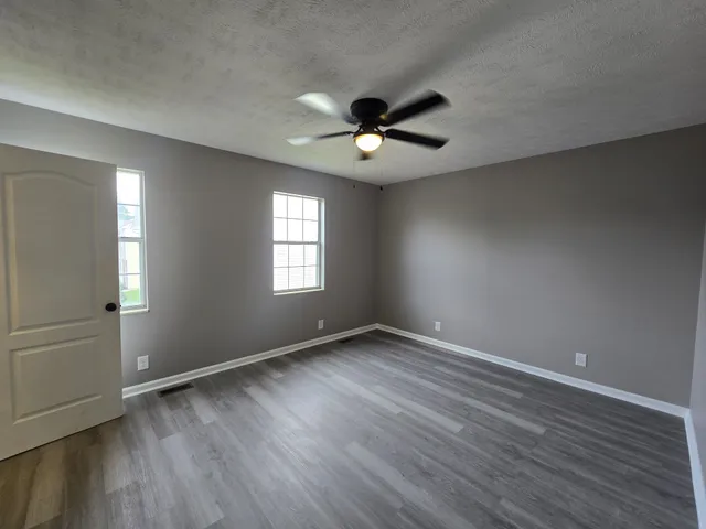 an empty room with wooden floor fan and windows