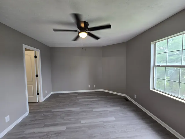 an empty room with wooden floor fan and windows